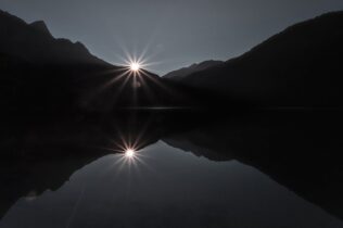 The sun behind a mountain near a body of water